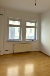 Blick in einen leeren Raum mit 2 Fenstern und einem Heizkörper. Parkettboden