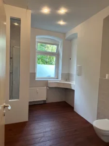 Blick in ein leeres Badezimmer mit hellen Wänden und einem dunklen Boden